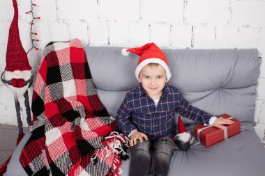 little boy in santa hat near christmas gnome toy, holding dwarf toy in hand in grey room. christmas decor and toys. kids playing