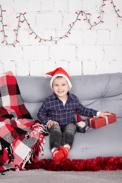 Маленький хлопчик у капелюсі Санта поблизу різдвяної гном-іграшки, тримаючи карликову іграшку в руці в сірій кімнаті. Різдвяний декор та іграшки. діти грають — стокове фото