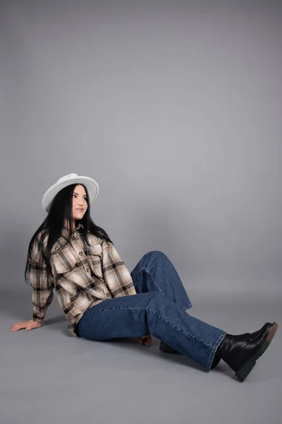 グレーの背景に白い帽子とジーンズを着た魅力的な若い女性。可愛い女性の肖像. — ストック写真