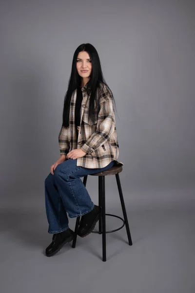 Porträtt av vacker ung kvinna i brun rutig skjorta och jeans på grå bakgrund. vacker kvinnlig porträtt — Stockfoto