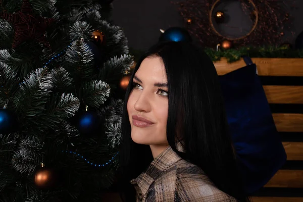 Confident beautiful young woman in plaid shirt near christmas tree. new year, winter theme — стоковое фото