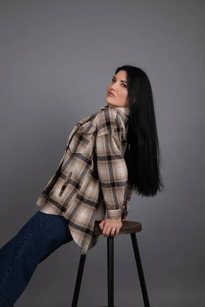 Portrait of beautiful young woman in brown checkered shirt and jeans on gray background. pretty female portrait — 图库照片