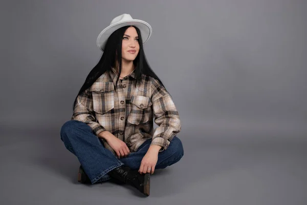 Retrato de bela jovem mulher em camisa xadrez marrom e jeans em fundo cinza. Retrato feminino bonito — Fotografia de Stock