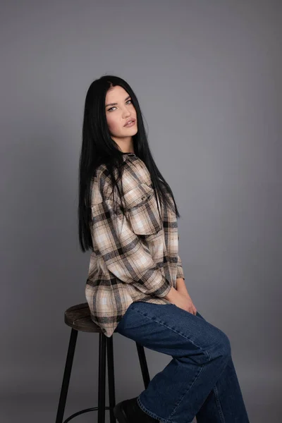 Portrait of beautiful young woman in brown checkered shirt and jeans on gray background. pretty female portrait — стоковое фото