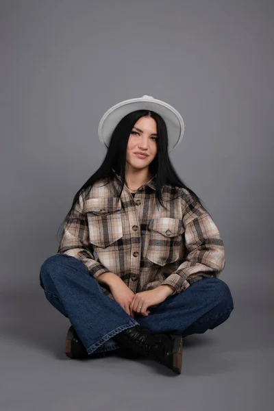 Attractive young woman in plaid shirt, white hat and jeans on gray background. pretty female portrait. —  Fotos de Stock