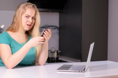 Yeşilli genç iş kadını akıllı telefon kullanıyor. Masada dizüstü bilgisayar var. Kız çalışıyor, internetten öğreniyor. Sosyal medya, ağ. Online pazarlama, eğitim.