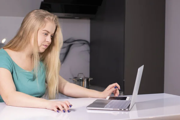 Mujer rubia joven seria que estudia desde casa en línea durante un brote de virus de cuarentena. trabajando en un portátil en su habitación gris. Primer plano. Quédate en casa. Resuelve problemas con el trabajo. Copiar espacio —  Fotos de Stock