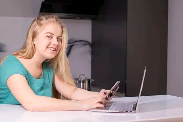 Joven empresaria en verde usando smartphone. En el escritorio está el portátil. Chica trabajando, aprendiendo en línea. Redes sociales, red. Marketing online, educación. —  Fotos de Stock