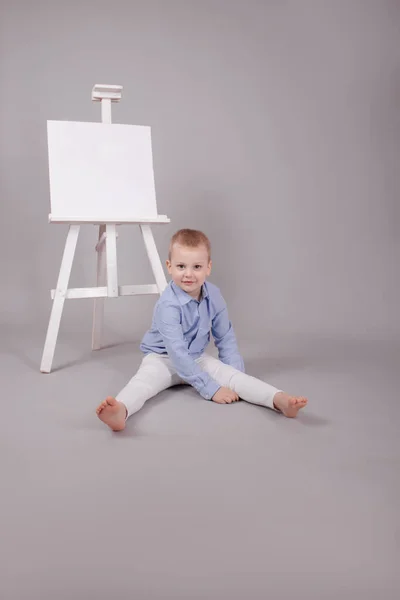 Malý chlapec stojící u stojanu na prezentaci s prázdným plátnem. Izolované na šedém pozadí. Prázdná maketa — Stock fotografie