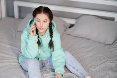 Uzaktan kumandalı ya da evden uzak çalışmalı. Genç esmer kadın blogcu yatakta turkuaz modern telefonla. Karantina kısıtlamaları. covid-19 salgını