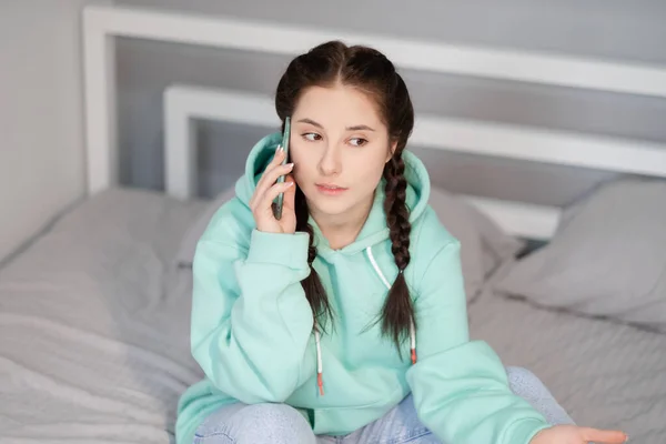 Uzaktan kumandalı ya da evden uzak çalışmalı. Genç esmer kadın blogcu yatakta turkuaz modern telefonla. Karantina kısıtlamaları. covid-19 salgını — Stok fotoğraf