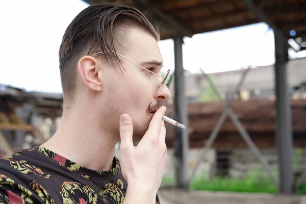 Jovem homem confiante com bigode fumando um cigarro lá fora. mau hábito, vício em tabaco — Fotografia de Stock