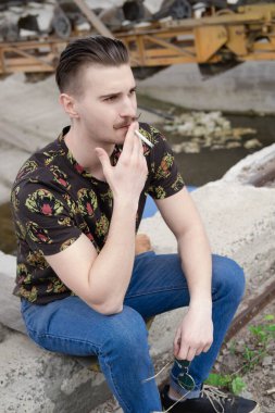 Dışarıda sigara içen bıyıklı, kendine güvenen genç bir adam. Kötü alışkanlık, tütün bağımlılığı