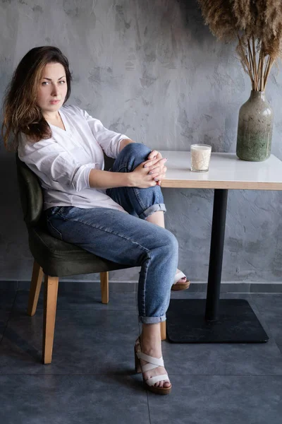 Красива дівчина брюнетка в білій блузці і джинсах в інтер'єрі лофт-кафе. перерва на каву. щасливий працівник . — стокове фото