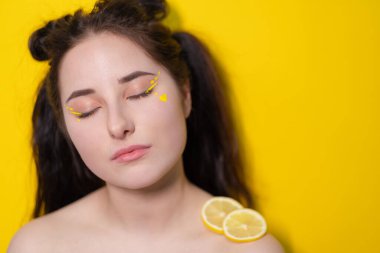 Limon dilimli genç bir kadın, sarı arka planda limon tutan çıplak omuzlu esmer bir kız. Turunçgiller, sağlıklı yiyecekler. Lezzetli meyve.