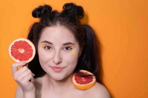 Chica joven con rodaja de pomelo sobre fondo naranja — Foto de Stock