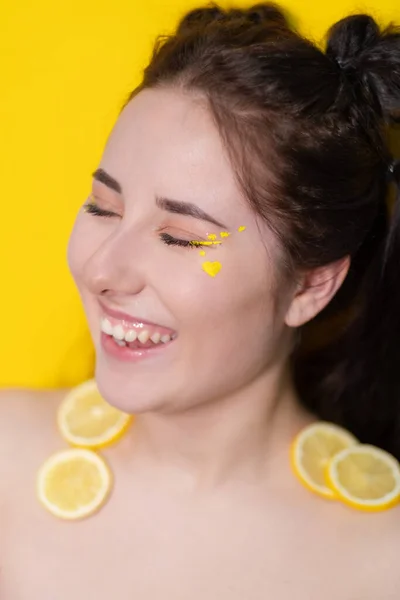 Brunette woman girl with lemon near skin face on yellow background. tasty juicy fruit. Tropical fruits, Healthy food. citrus slice — Stock Photo, Image