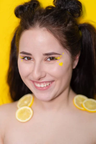 Mujer joven con rodajas de limón, chica morena con hombros desnudos sosteniendo limón cerca de la cara sobre fondo amarillo. cítricos, comida saludable. fruta jugosa sabrosa. — Foto de Stock
