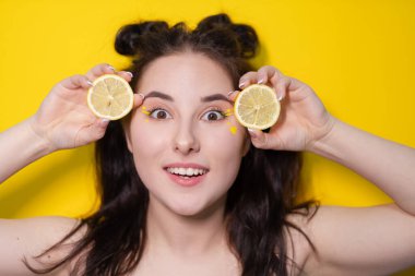 Limon dilimli genç bir kadın, sarı arka planda limon tutan çıplak omuzlu esmer bir kız. Turunçgiller, sağlıklı yiyecekler. Lezzetli meyve.