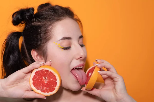 Сладкая радостная брюнетка женщина женщина с обрезанным ломтиком грейпфрута возле лица кожи на оранжевом фоне. вкусные сочные фрукты. Тропические цитрусовые, здоровая пища. потеря веса — стоковое фото