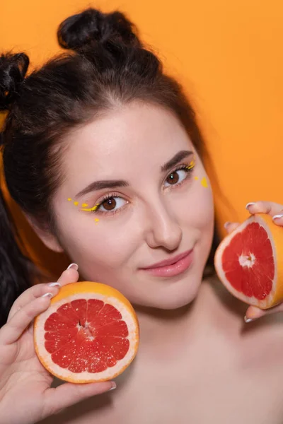 Chica joven con rodaja de pomelo sobre fondo naranja —  Fotos de Stock