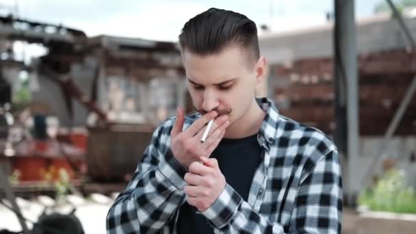 Jonge knappe man met snor in geruit zwart-wit shirt die buiten een sigaret rookt. slechte gewoonte — Stockvideo