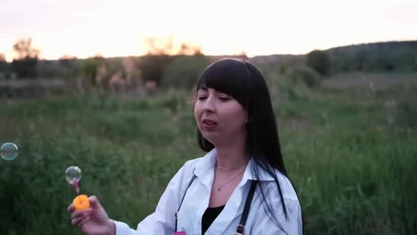 Smuk ung kvinde gør sæbebobler i sommer grønne felt på solnedgang. lykkelig fredelig tid. tusindårsgeneration – Stock-video