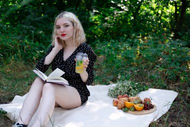 Parkta piknik yapan genç bir kadının portresi. Lezzetli atıştırmalıklarla dolu bir kitap okuyor..