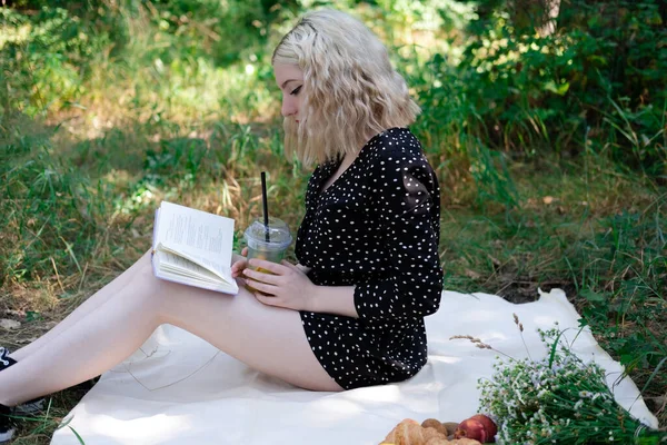 Parkta piknik yapan genç bir kadının portresi. Lezzetli atıştırmalıklarla dolu bir kitap okuyor..