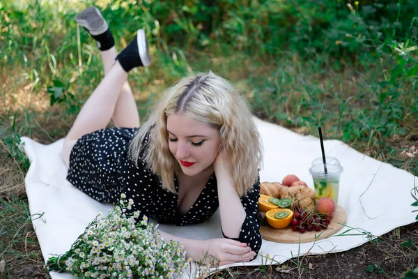 Parkta ekose bir piknikte lezzetli atıştırmalıklarla güzel sarışın bir kadın. Limonata, meyve ve kruvasan. Yaz zamanı, dinlen, rahatla, tadını çıkar. özgürlük.