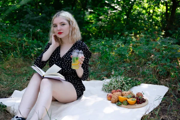 Parkta piknik yapan genç bir kadının portresi. Lezzetli atıştırmalıklarla dolu bir kitap okuyor..