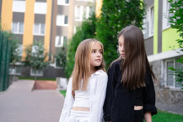 fraternal twins sisters. blonde and brunette teen girls in fashionable black and white clothes outdoors. sisterhood, siblings spending time together