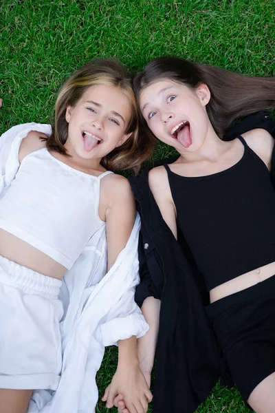 fraternal twins sisters. blonde and brunette teen girls in fashionable black and white clothes outdoors. sisterhood, siblings spending time together