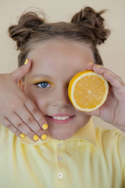 Sweet cute girl school age holding a ripe fresh lemon on yellow background. child with fruit on colorful background. summer citrus food — Foto de Stock