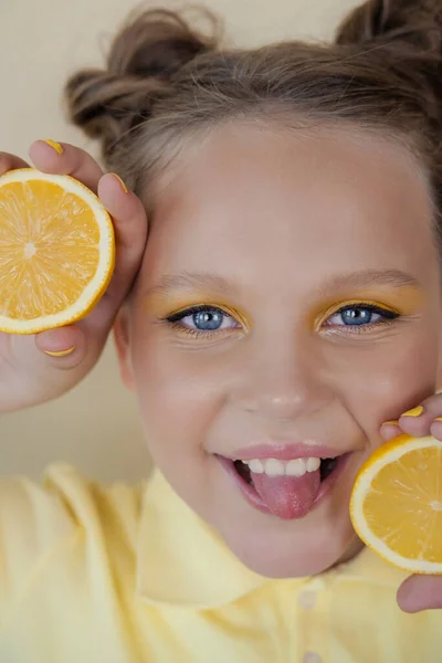 Sweet cute girl school age holding a ripe fresh lemon on yellow background. child with fruit on colorful background. summer citrus food — Stock Photo, Image