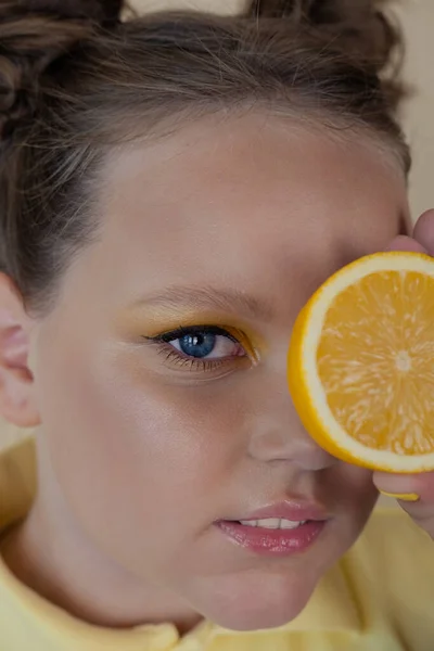 Charming tween girl with slices of ripe lemon on yellow background. juicy fruit concept. summer — Stock Photo, Image