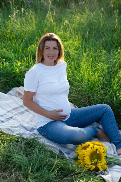 Yazın hamile. Dışarıda bir kutu ayçiçeğiyle mutlu ve hamile bir kadın doğanın tadını çıkarıyor..