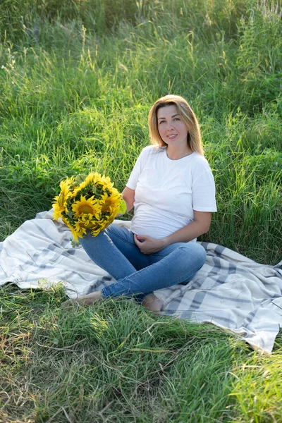 Yazın hamile. Dışarıda bir kutu ayçiçeğiyle mutlu ve hamile bir kadın doğanın tadını çıkarıyor..