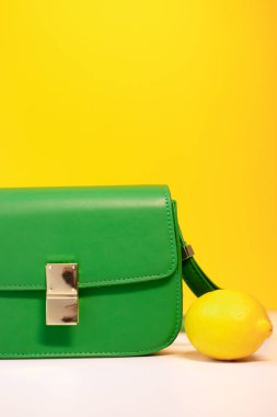 Zarif yeşil çanta ya da sarı arka planda limonlu el çantası. Ürün kompozisyon fotoğrafçılığı. Kadınlar için torba ve retiküle.