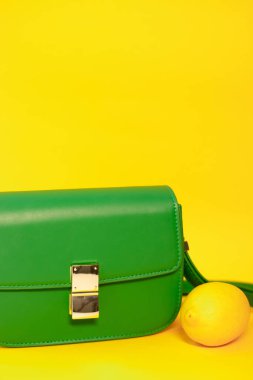 Zarif yeşil çanta ya da sarı arka planda limonlu el çantası. Ürün kompozisyon fotoğrafçılığı. Kadınlar için torba ve retiküle.