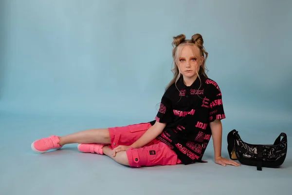 fashion teenager portrait. tween school girl with orange makeup wearing pink stylish cool clothes on blue background.