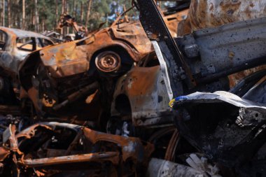 Ukrayna 'nın sembolü olarak bilezik. Mavi ve sarı renkli bayrak. Arka planda Rus saldırısından kalma yanmış arabalar. Ukrayna 'ya karşı işlenen Rus askeri suçları. Ukrayna 'nın zaferi.