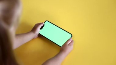 Yakın çekim anaokulu kızı elinde yeşil ekran planlı akıllı telefon tutuyor. Şablon video malzemeleri. Sahte uzay telefonu kopyala. Renk Anahtarı, Görünüm İçeriği, Videolar, Tap on Screen, Play Online Games. Yavaş çekim.