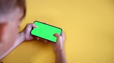 Yeşil ekran. Çocuk elinde bir Smartphone tutuyor. Yakın plan bir oyun oynuyor. Boş yeşil ekranlı telefon reklam için görüntüyü oluşturur. Yavaş çekim.