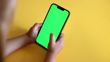 Preschool Girl Use Smartphone With a Green Screen Layout. Chroma key mock-up on smartphone in hand. Color Key. Watching content, Videos, photos, playing a game. Slow motion.