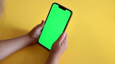 Preschool Girl Use Smartphone With a Green Screen Layout. Chroma key mock-up on smartphone in hand. Color Key. Watching content, Videos, photos, playing a game. Slow motion.