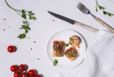 Domates soslu lahana ruloları, beyaz tabakta az miktarda malzeme, ekşi krema ve biber ve beyaz keten peçete. Bir rulo kesiliyor. Beyaz desenli taş zemin. Düz yatıyordu. Yatay yönelim.