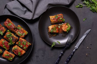 Domates soslu lahana ruloları ve tavada maydanoz dilimleri ve siyah tabakta. Dut, çatal ve bıçak yemeye hazır bez peçete dokulu siyah taş arka planda yatıyordu..