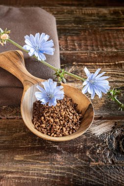 Tahıl taneleri yığını ve ahşap kaşıkta mavi hindiba çiçeği kaba, kahverengi, çatallı tahta masa üzerinde. Keten tekstil peçete ve bitki sapı yan yana çiçek açıyor. Dikey yönelim.