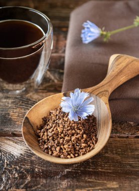 Anında granüller, mavi hindiba bitkisi çiçek açar ve kahverengimsi doğal ahşap masa üzerinde termik bardakta kahve alternatifi içmeye hazırdır. Keten tekstil peçetesi yanında. Dikey yönelim.